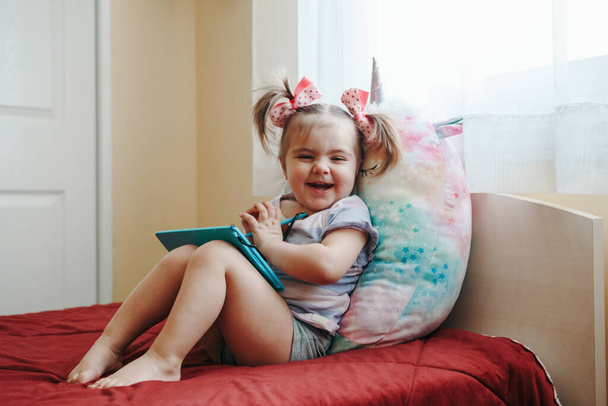 Divertido lindo niño sonriente niña dibujo con lápiz en la tableta digital de la almohadilla de dibujo. Niño pequeño usando tecnología. Desarrollo de la educación temprana. Feliz hogar auténtico estilo de vida infancia. - Foto, imagen