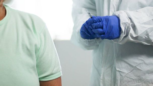 Mavi lateks eldivenli doktor şırıngayı cam şişeden doldurup Coronavirus, grip ve kızamık hastalıklarına karşı laboratuardaki yaşlılara iğne yapacak. - Fotoğraf, Görsel