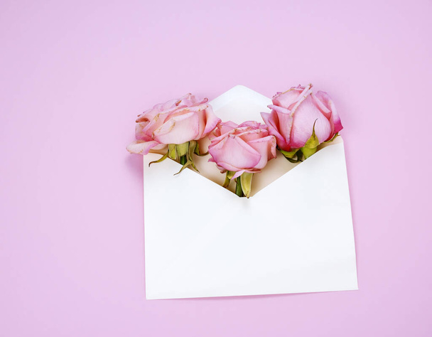 Top view flat lay white envelope with pink roses pink background - Foto, imagen