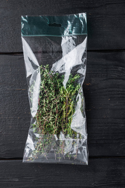 Thyme in plastic bag set, on black wooden table background, top view flat lay - Foto, imagen