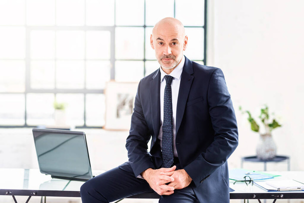 Portré egy vezető üzletemberről, aki öltönyt és nyakkendőt visel, miközben az irodában ül.. - Fotó, kép