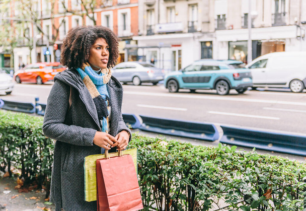 Afro fille de style va faire du shopping dans une ville et porte des sacs colorés - Photo, image