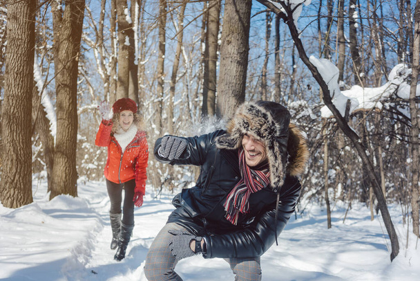 Kadın kışın neşeli bir şekilde erkeğine kartopu atıyor. - Fotoğraf, Görsel
