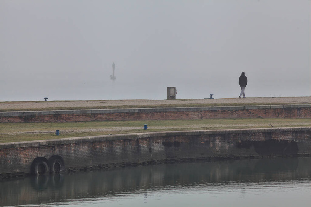 イタリアの町の霧の日に湖の古代の桟橋を歩く男 - 写真・画像