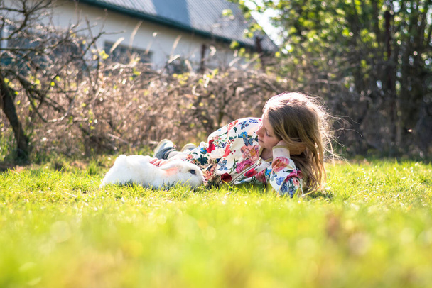 dziewczynka z białym królikiem zwierzakiem bawiącym się w ogrodzie - Zdjęcie, obraz