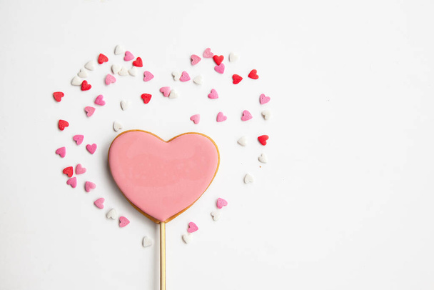 Dulce corazón en un palo sobre un fondo blanco. Galletas rosadas para San Valentín - Foto, imagen