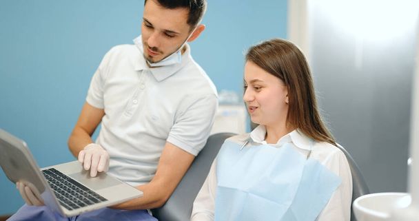 Dentista mostrando foto de dientes en un portátil para un paciente joven - Foto, imagen