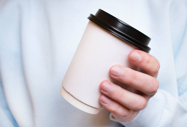 Close up of a hand of man holding a coffee cup beside a window with a green background outside - Foto, Imagem
