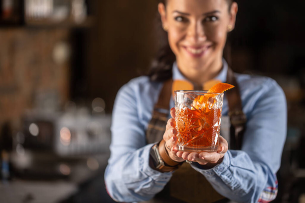Old fashioned drink in ornamental glass offered by a female bartender in a pub. - Zdjęcie, obraz