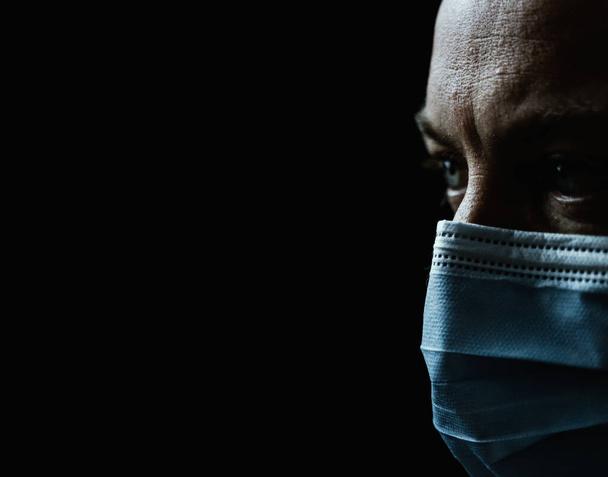 Close up portrait of a white man wearing a face mask and looking worried. Shallow depth of field isolated on black background. High quality photo - Photo, Image