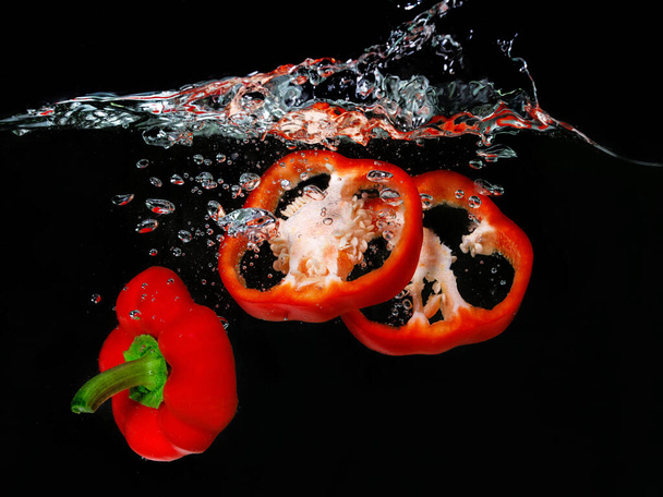 czerwona papryka wpadająca do wrzącej wody na ciemnym tle. Podwodny widok. Gotowanie, wegetariańskie, gotowanie w domu koncepcja - Zdjęcie, obraz