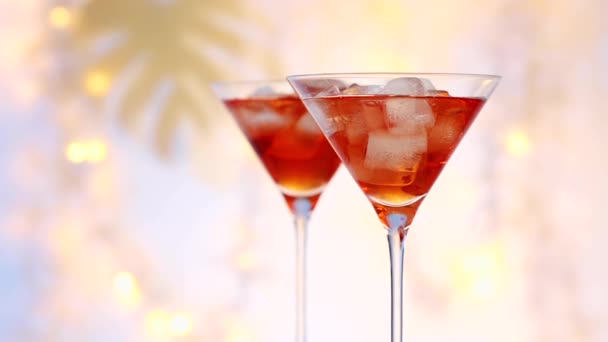 twee glazen rode zomer cocktail met ijsblokjes close-up zoom in, onscherpe feestelijke lichten op de achtergrond - Video