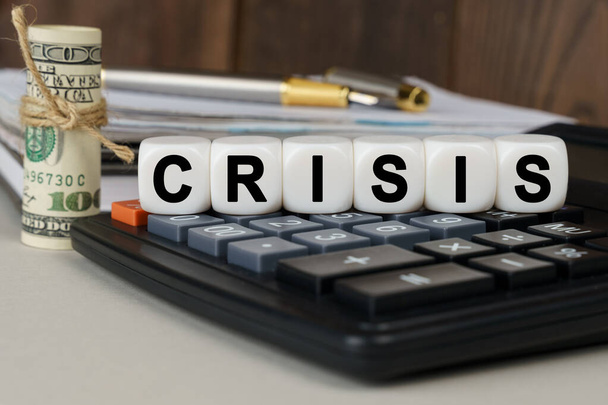 Business and finance concept. There are cubes on the calculator that say - CRISIS. Nearby out of focus - dollars, notebook and pen - Fotoğraf, Görsel