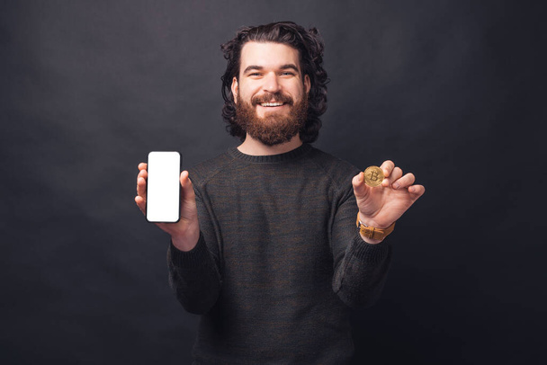 Retrato de hombre guapo sonriente en pantalla de teléfono casual y bitcoin - Foto, Imagen