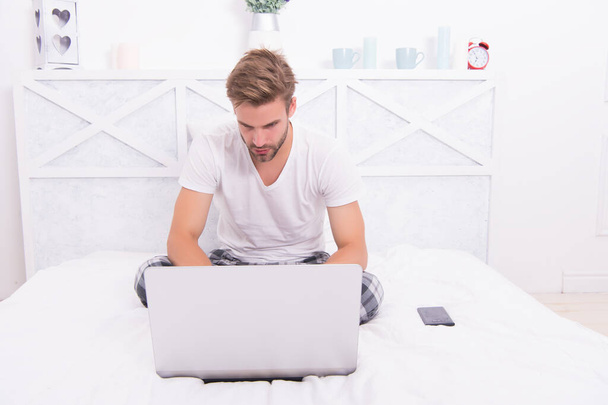 Handsome guy in pajamas use laptop modern technology for working from home during COVID-19, telework - Foto, Imagen