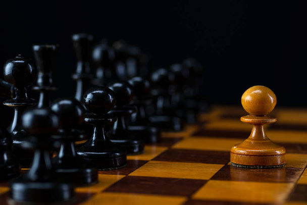 One white pawn against an army of black pieces on a chessboard - Zdjęcie, obraz