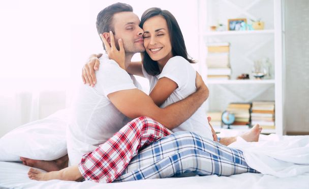 Excited and happy young smiling beautiful couple in love relaxing at home on the bed while they hug each other and having fun - Foto, imagen