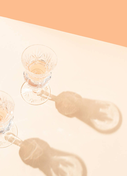 Два бокала вина с солнечными дневными тенями на ярко-бежевом и оранжевом фоне. Творческая летняя концепция. - Фото, изображение