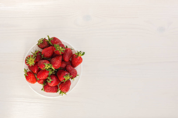 Aardbeien op een witte houten achtergrond bovenaanzicht. Rode rijpe aardbeien op een wit bord. Het concept van gezond eten, zomervitamines. Vegetarisch eten, zoet dessert. Vlakke lay-out, kopieerruimte - Foto, afbeelding
