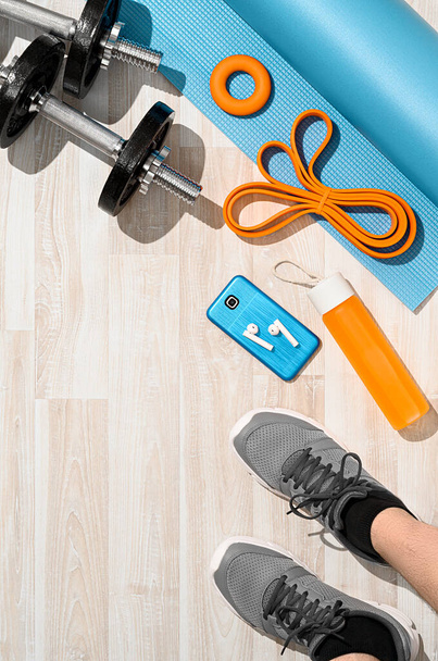 Workout at home concept. Overhead view of male legs in sports shoes with fitness outfit and smartphone on wooden floor. Morning training, sunlight. Place for text, top view, vertical orientation - Photo, Image