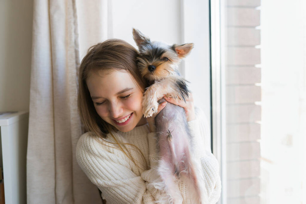 Fiatal nő játszik kutyával hétvégén otthon. Boldog yorkshire-i terrier kiskutya - Fotó, kép