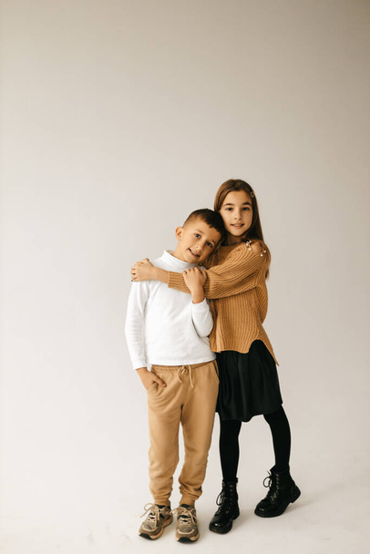 Cute girl and boy on a gray background are back to each other, arms crossed and smiling. High quality photo - Foto, immagini