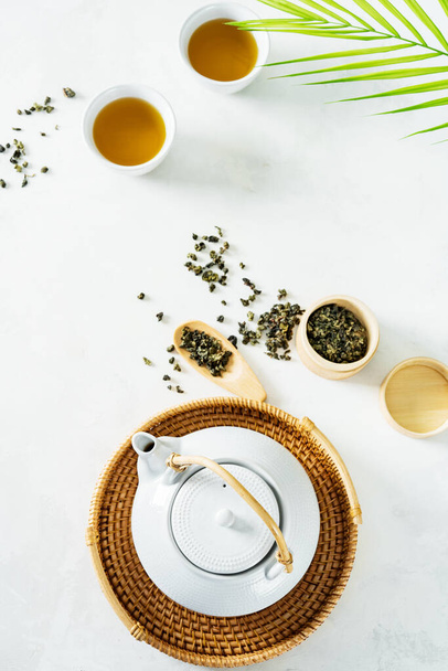Asian tea concept, two white cups of tea and teapot surrounded with green tea dry leaves view from above, space for a text on white background - Foto, imagen