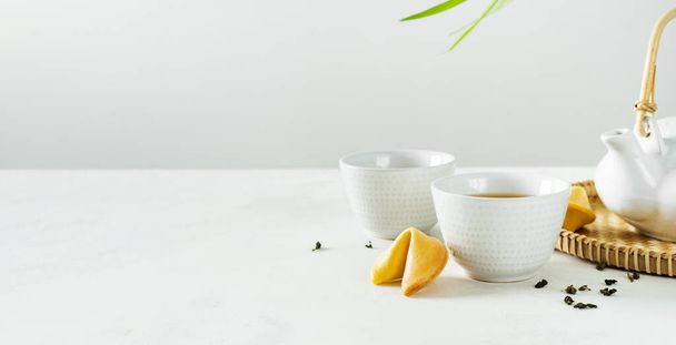 Aziatische lifestyle mockup tea concept, twee witte kopjes thee en theepot omgeven door groene droge thee met ruimte voor een tekst op lichte achtergrond. Breed spandoek. - Foto, afbeelding