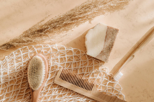 Zero waste bathroom accessories hairbrush, bamboo toothbrush, loofah and natural soap in reusable shopping bag on beige background. Top view. Vintage color filter - Photo, image