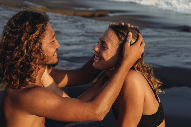 A bright couple in love admires each other the man strokes the girls hair and they gently look at each other against the background of the ocean rolling their waves - Foto, Imagem