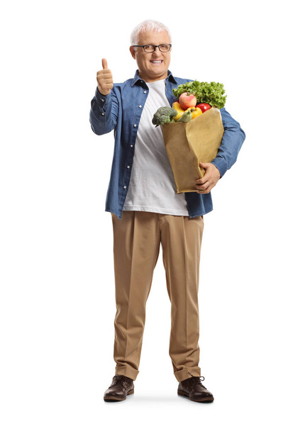 Full length portrait of a mature man with a grocery bag showing thumbs up isolated on white background - Foto, Bild