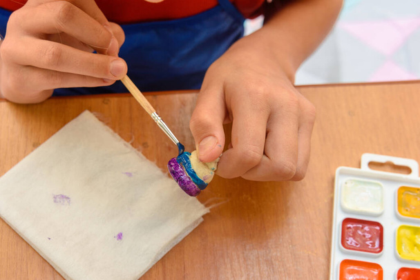 Ένα κορίτσι ζωγραφίζει ένα ειδώλιο από ζύμη αλατιού με ένα πινέλο - Φωτογραφία, εικόνα