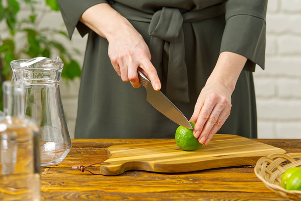 Γυναίκα κοπή ασβέστη στην κουζίνα, λεμόνι νερό, Δροσιστικό νερό με ασβέστη και λεμόνι, υγιεινή διατροφή έννοια - Φωτογραφία, εικόνα