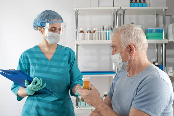Enfermera sosteniendo una carpeta de portapapeles, dándole un frasco de pastillas naranjas a un adulto mayor. Caso de atención médica del hospital de cita del médico - Foto, imagen