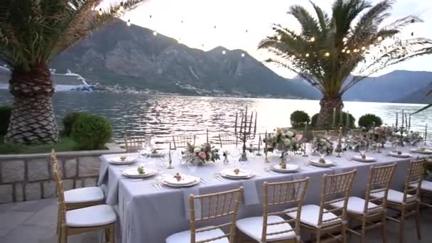Stůl na svatební hostině, zdobený květinami, svícny a mladými granátovými jablky na molu v zátoce Kotor - Záběry, video