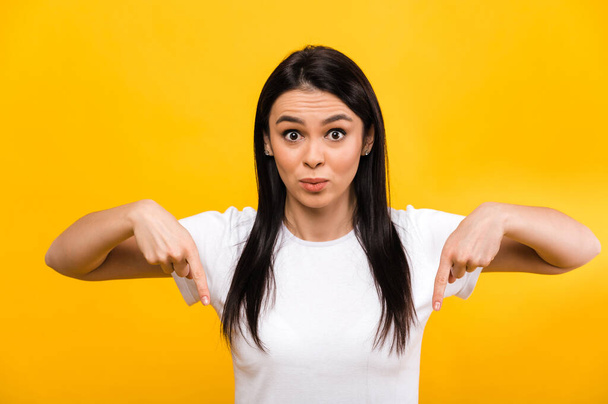 Photo of surprised excited cute caucasian girl pointing fingers down, standing on isolated orange background, with shocked face and looks at the camera - Photo, Image