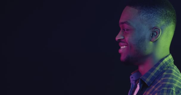 Profil portré fiatal fekete férfi néz másolás tér és mosolygós, neon fények háttér, szabad hely a mockup - Felvétel, videó