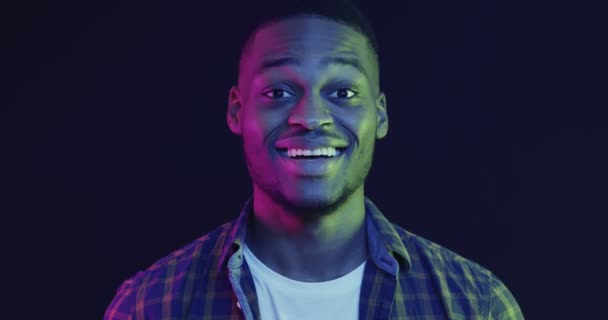 Hombre afroamericano que se siente sorprendido y sorprendido, rostro conmovedor en la emoción y la risa, fondo luces de neón - Metraje, vídeo