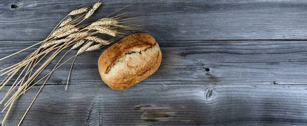 Top view of homemade full sourdough loaf of bread with dried wheat stalks on weathered wooden planks  - 写真・画像