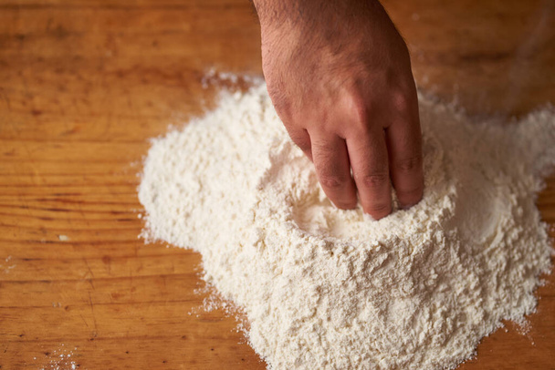 a cook's hands make a flour volcano on a wooden table - Zdjęcie, obraz