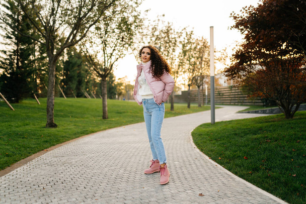 Girl walks in the park, dressed in jeans and a pink jacket - Zdjęcie, obraz