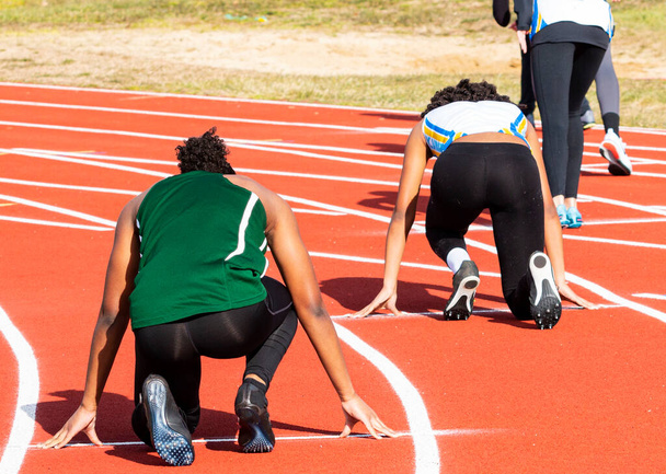 Achteraanzicht van vrouwelijke sprinters op hun plaats klaar om hun sprint-hardloopwedstrijd met spandex op een buitenbaan te beginnen. - Foto, afbeelding