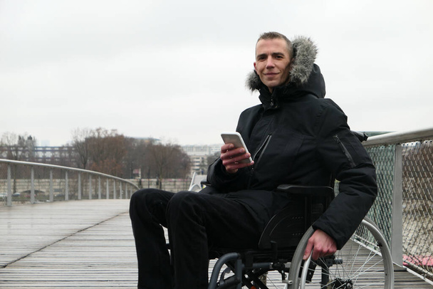 Engelli kişi kavramı. Sokakta tekerlekli sandalyedeki adam. İnsanlar akıllı telefon teknolojisi kullanıyorlar.. - Fotoğraf, Görsel