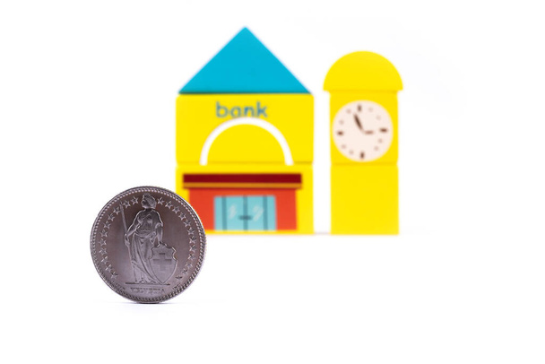 Moneta o wartości 1 franka szwajcarskiego przed tradycyjnym budynkiem banku wykonanym z kostek dziecięcych na białym tle - Zdjęcie, obraz