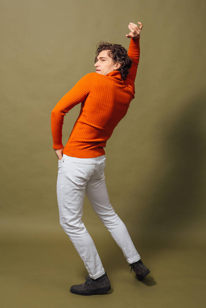 Full lengh portrait of a tall handsome man dressed in orange turtleneck and white jeans posing on the green background - Fotografie, Obrázek