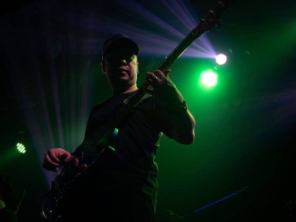 Aasialainen muusikko, basisti, joka soittaa bassokitaraa lavalla vihreällä valolla tummalla taustalla. Musiikkiesitys rock-yhtyeen konsertissa. - Valokuva, kuva