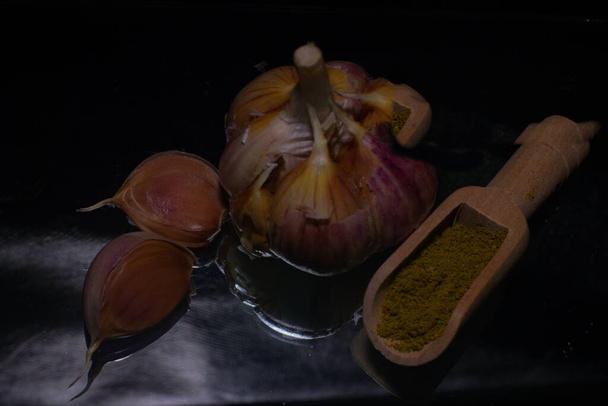 garlic on a black background next to a spatula with seasonings. High quality photo - Foto, Imagen