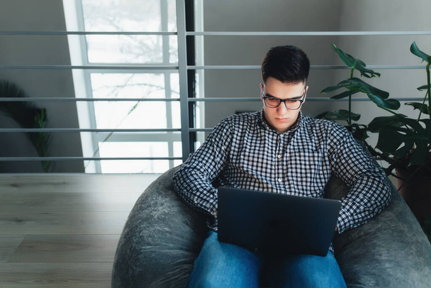 Man using laptop, wearing glasses, cushioned furniture. Blurred background - Photo, Image