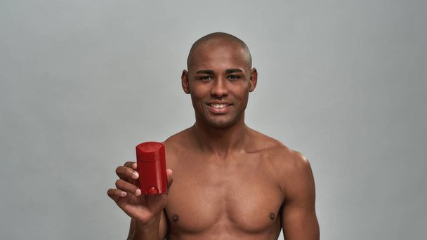 Cheerful man presenting a deodorant in a red packaging - Фото, изображение