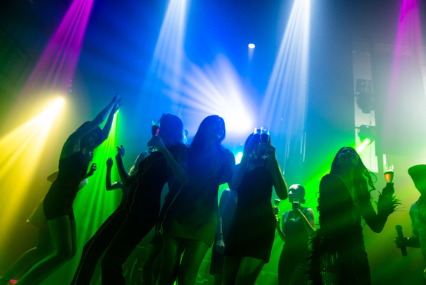 Silhouette image of people dance in disco night club to music from DJ on stage - Photo, Image